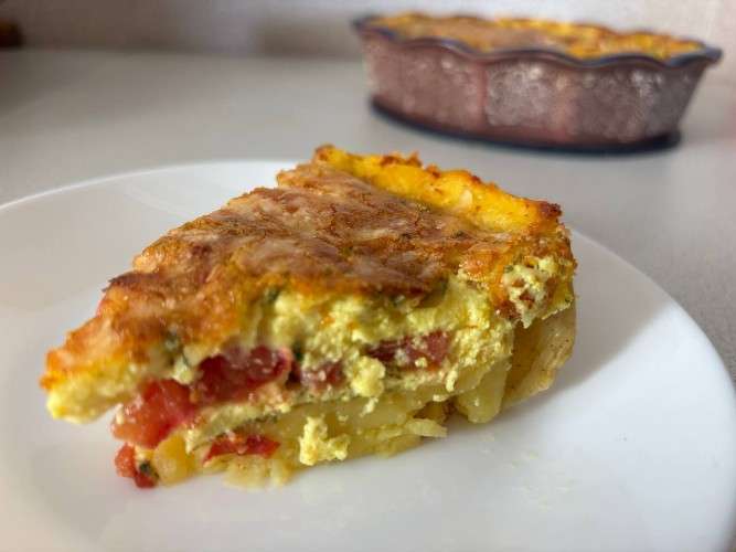 Кусок картофельного пирога с помидорами и сыром
