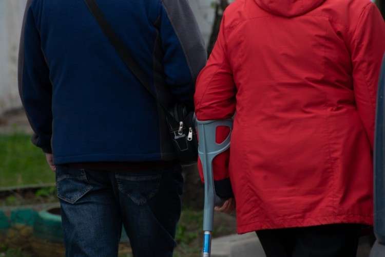 пенсионерка с костылём в сопровождении мужчины