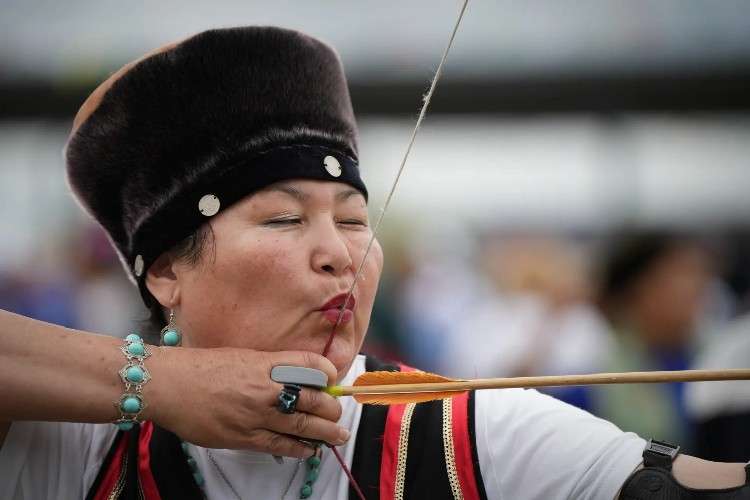 Женщина в нациальном костюме стреляет  из лука