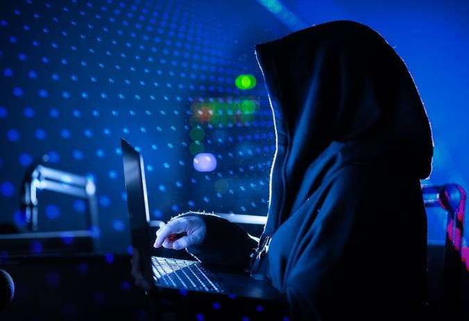 Человек в черном капюшоне перед ноутбуком