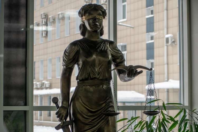 Скульптура Фемиды на фоне окна и комнатного растения