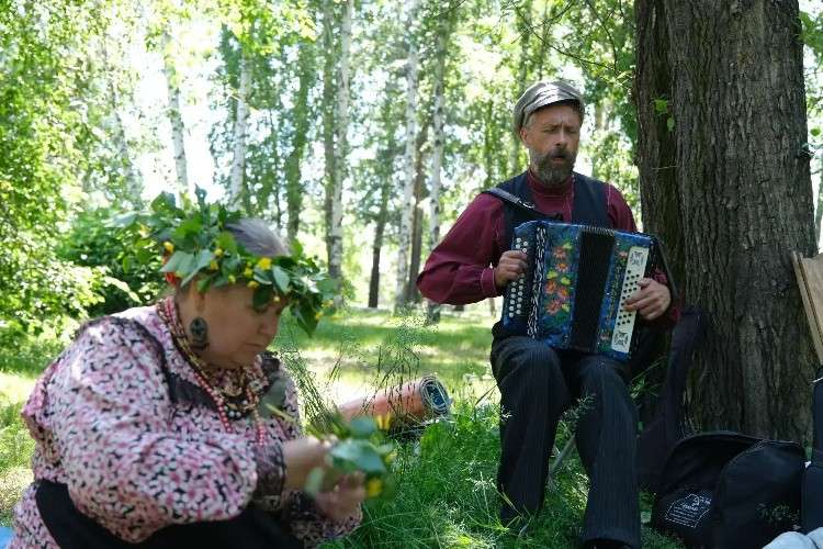 Мужчина играет на баяне, женщина рядом плетёт венок
