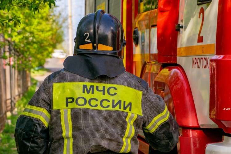сотрудник МЧС спиной к зрителю движется к пожарной машине перед ним