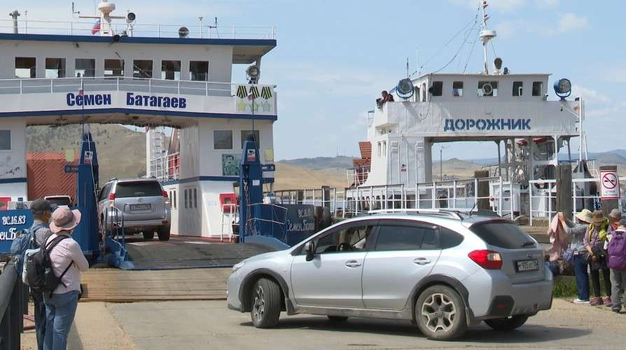 Паромная переправа. Автомобиль заезжает на белый паром «Семен Батагаев». Рядом стоит второй паром «Дорожник». У трапа находятся люди, на берегу — серебристый автомобиль. Солнечный день.