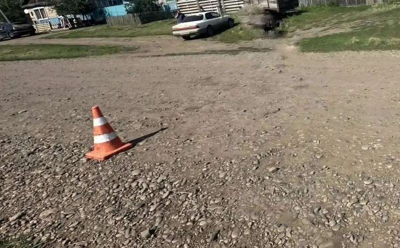 Пустынный участок с каменистой и песчаной почвой. На переднем плане слева стоит оранжевый дорожный конус с белыми полосами, отбрасывающий четкую тень.