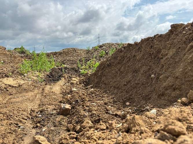 Низкий ракурс на разрытый участок земли. Справа возвышается крутой склон из рыхлой коричневой почвы. В центре — грунтовая колея с комьями земли