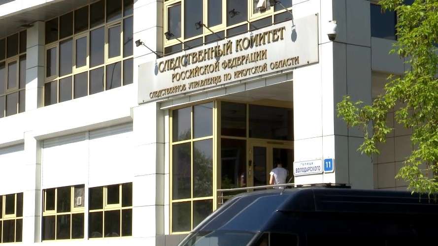 Белое административное здание с табличкой: «Следственный комитет Российской Федерации, Следственное управление по Иркутской области». У входа стоит мужчина в белой футболке, на стене висит указатель улицы «Володарского, 11».