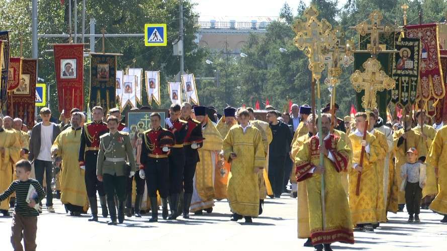 Религиозное шествие (крестный ход) по городской улице в солнечный день. Впереди идут священнослужители в золотистых парчовых облачениях, несут большие кресты и хоругви.