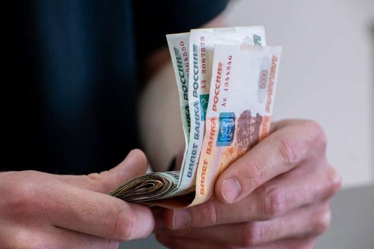 Руки человека держат веером несколько российских купюр номиналом 5000 рублей. Видны надписи «БИЛЕТ БАНКА РОССИИ» и серийные номера.