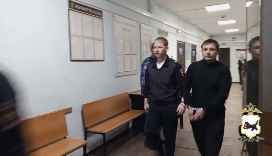 Мужчину ведут по коридору в наручниках.