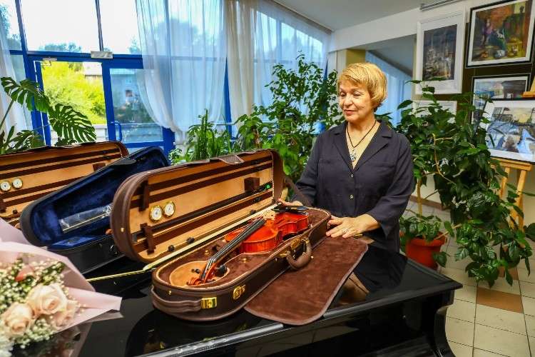 Женщина стоит около рояля. На инструменте лежит открытый кейс со скрипкой.