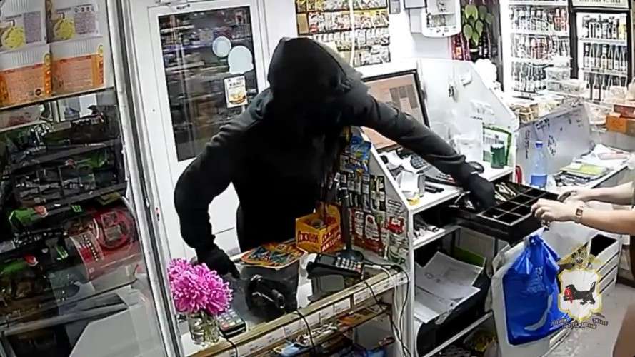 Человек в чёрном достаёт деньги из кассы в магазине