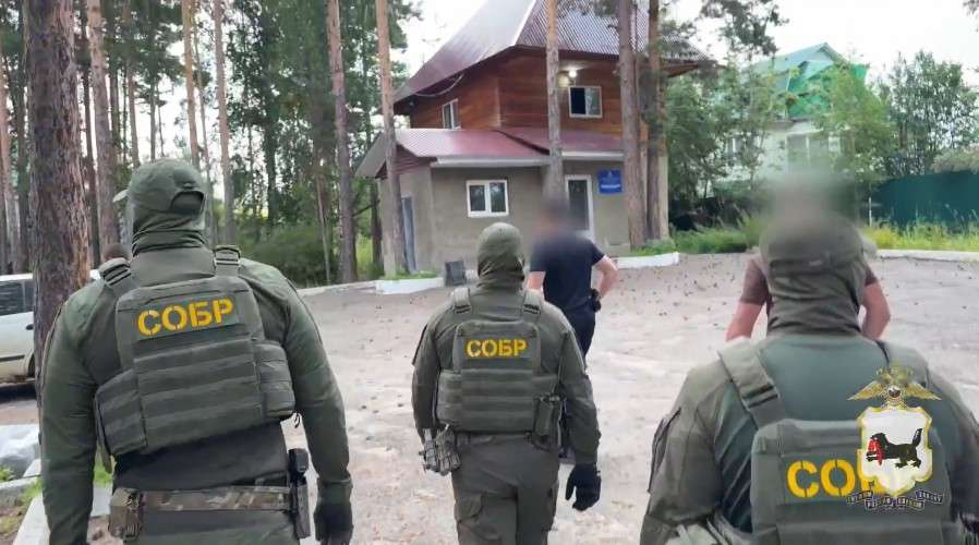 Трое мужчин в камуфляже и спецформе с надписями СОБР движутся в сторону дома за мужчиной в чёрных штанах и футболке