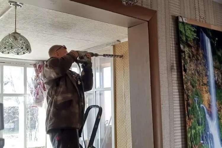 Человек сверлит дыру в стене