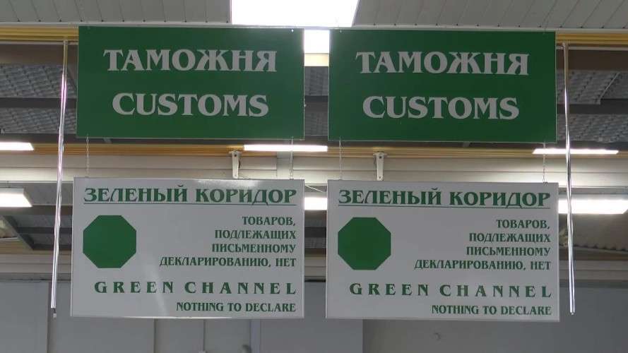 Два одинаковых информационных стенда висят под потолком в помещении таможенного контроля. Верхние зеленые таблички гласят «ТАМОЖНЯ / CUSTOMS».