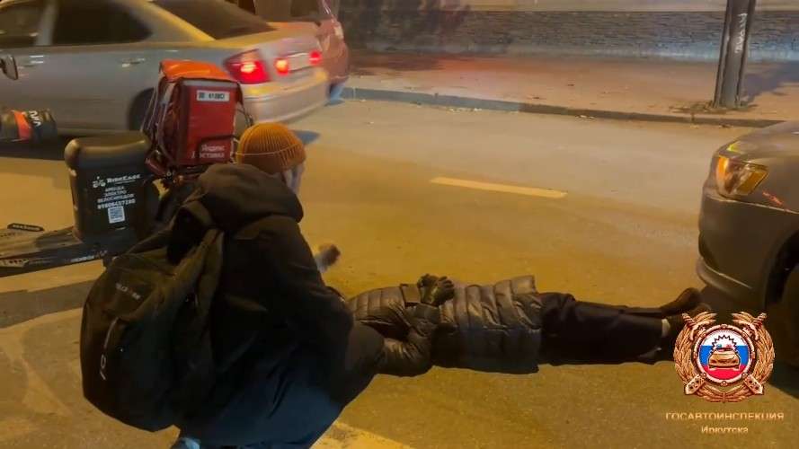 Женщина лежит на асфальте, рядом сидит мужчина