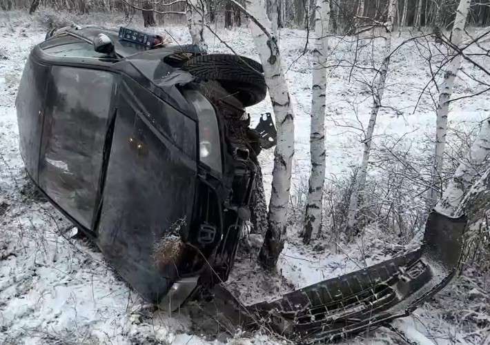 Чёрный автомобиль в кювете лежит на боку возле берёзы